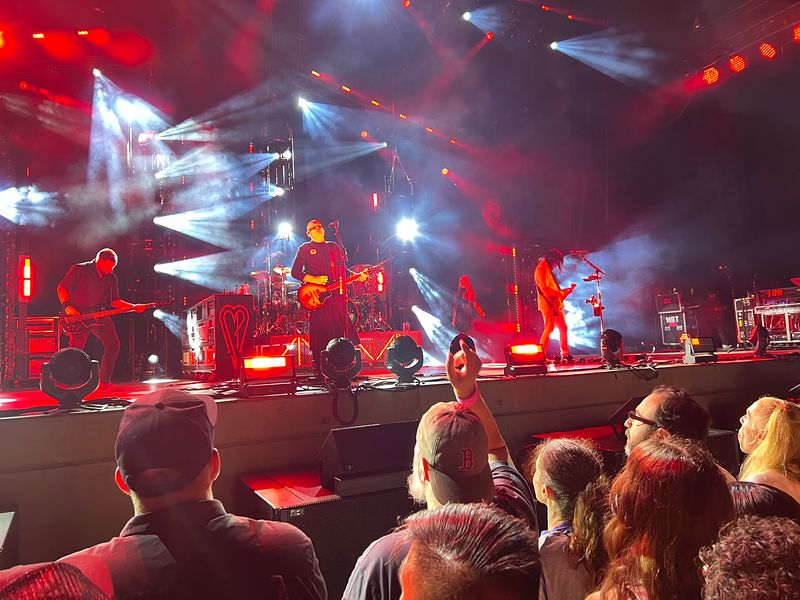 A band on a red-lit stage, seen over the crowd at an outdoor concert