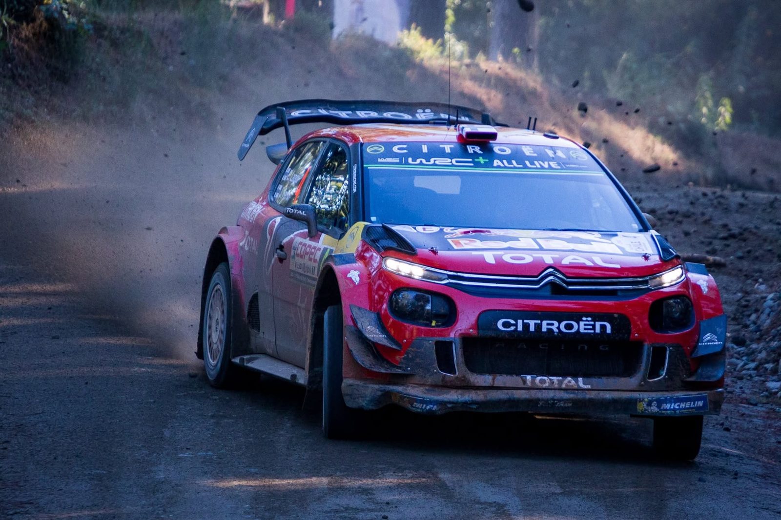 A Citroën C3 WRC sliding through dust and low sun on a forest stage at WRC Rally Chile 2019